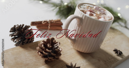 Feliz navidad text in red over pine cones, cinnamon and christmas hot chocolate with marshmallows