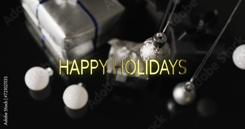 Happy holidays text over christmas baubles and presents on dark background