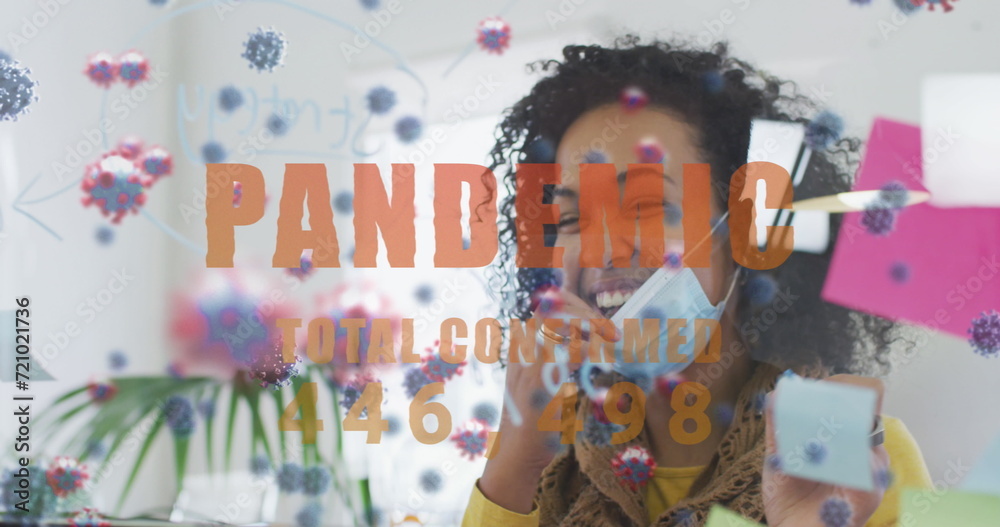 Fototapeta premium Image of word pandemic with covid cells floating and woman taking mask off