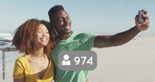 Profile icons with increasing numbers against african american couple taking a selfie on the beach