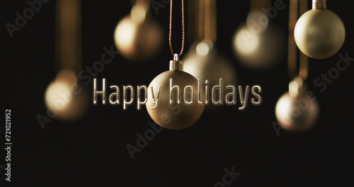 Happy holidays text with silver christmas baubles hanging on dark background