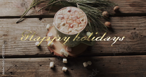 Happy holidays text in gold over christmas hot chocolate with marshmallows on wooden background