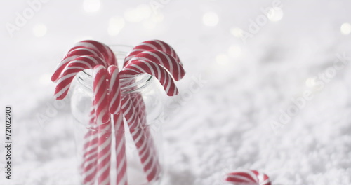 Candy canes in a jar set against a snowy backdrop, with copy space