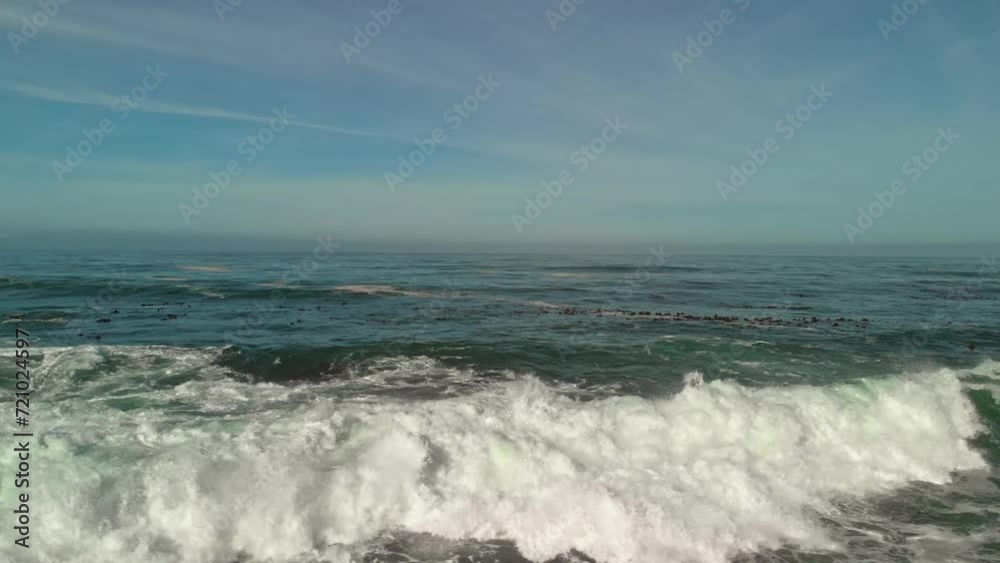 Low flying drone following a breaking wave panning with the wave revealing the shore with boulders, rocks, dunes, houses and beach. Low flying drone following a breaking wave panning with the wave revealing the shore with boulders, rocks, dunes, houses and beach.