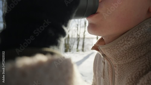 Close-up of person sipping from a thermal mug on a snowy day. photo