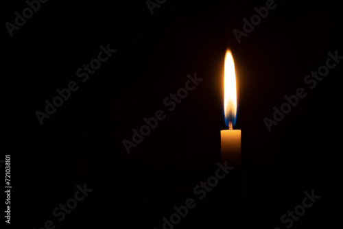 A single burning candle flame or light glowing on an orange candle on black or dark background on table in church for Christmas, funeral or memorial service with copy space