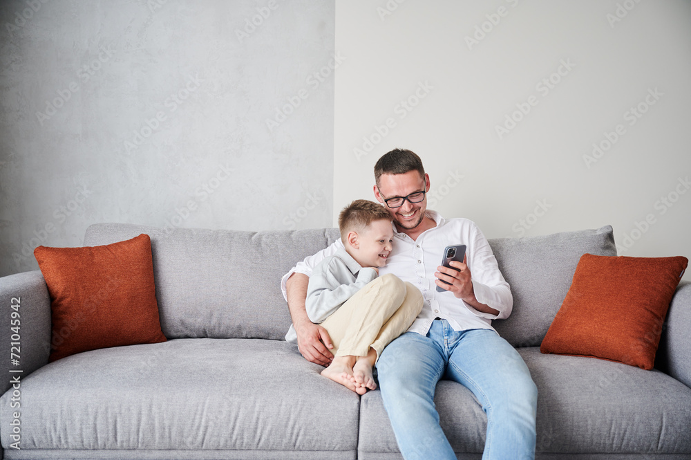 Cute moment of dad and little kid playing smartphone. Father in glasses showing son funny videos. Handsome man and his son laughing at funny picture.
