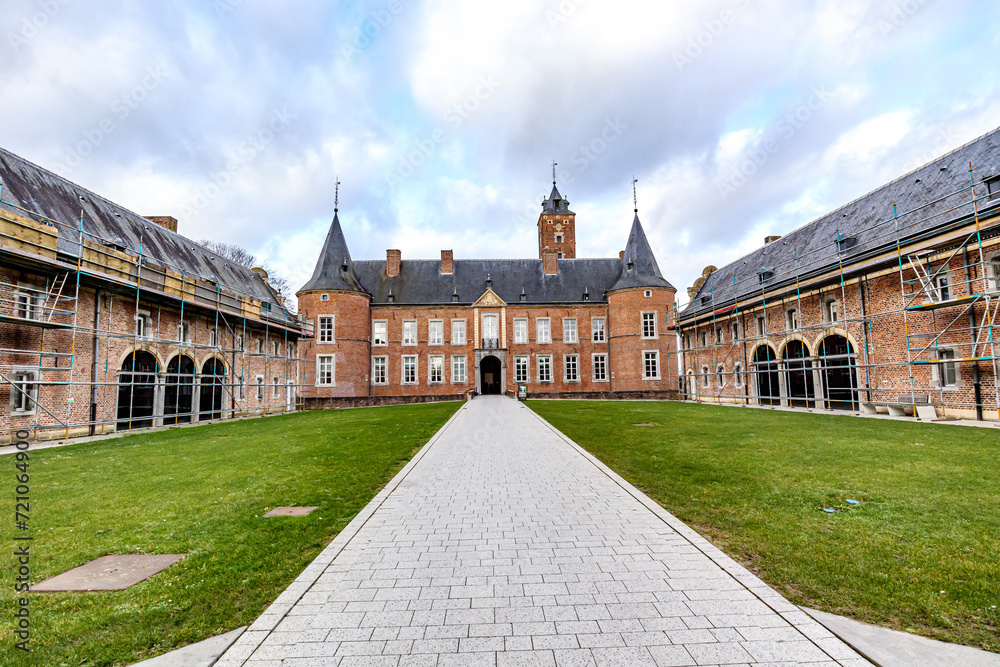 Straight path in outer courtyard in direction of Alden Biesen Castle between side buildings, rear facade, brick walls, gable roof and two towers, 16th century, cloudy day in Bilzen, Limburg, Belgium