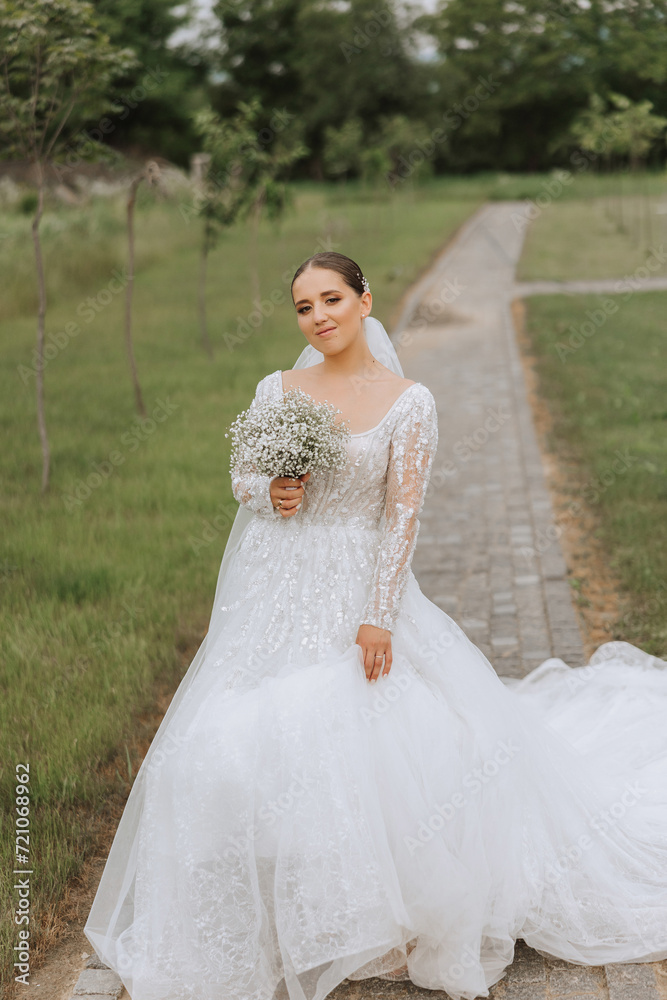 Beautiful bride with a long train. The bride in a white dress with a long train in nature on a summer day. Summer wedding.