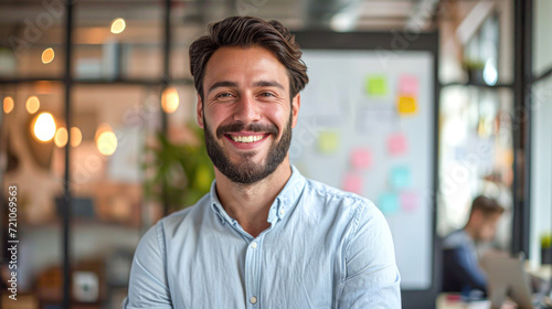 Cheerful young entrepreneur with a warm smile working on his laptop in a casual, creative office space with colorful sticky notes in the background.