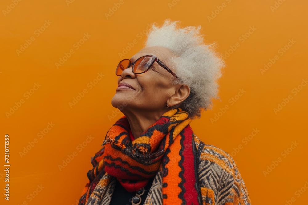 Joyful senior woman in stylish glasses and autumn attire against vibrant orange backdrop. Warm, fashionable, lively.