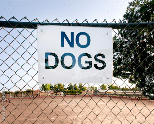 No dogs Allowed on a chain link fence at a park with a dirt playing field