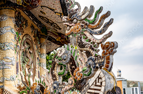 stunning dragon sculpture with vibrant mosaic tiles, graces rooftop of pagoda as captivating architectural element. intricate details and rich colors. adding touch of elegance to sacred structure © Celt Studio