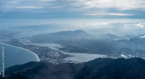 Captured from an airplane, this image showcases bird's-eye view of mountains, water bodies, villages, and small towns, all bathed in soothing blue tones. peaceful photo of nature and civilization