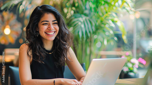 A radiant entrepreneur enjoys working on her laptop at a bustling cafe, her smile reflecting the satisfaction of a successful freelance career. © Kowit