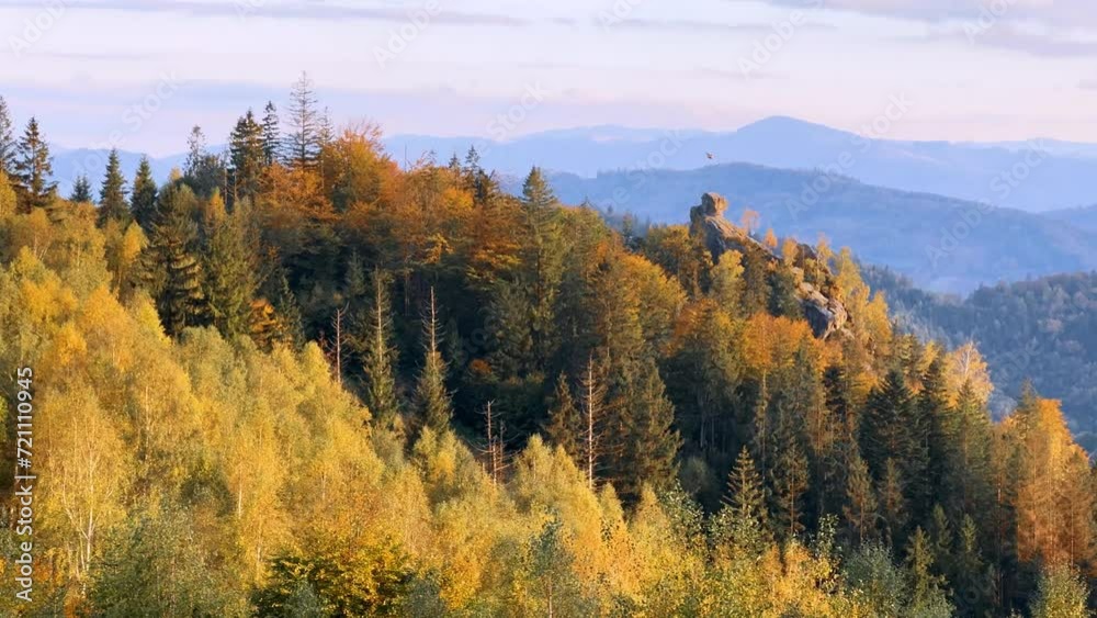 Sokil rocks over the peaks of the mountainous Carpathian region with an autumn pattern of red beech and yellow birch trees on the tops, river valleys with houses Sokil rocks over the peaks of the mountainous Carpathian region with an autumn pattern of red beech and yellow birch trees on the tops, river valleys with houses