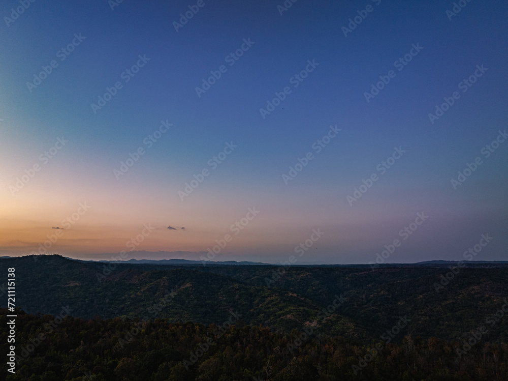 Aerial view A breathtaking sunset paints the sky with vibrant hues of orange and red, .casting a warm glow over the majestic mountains in a tranquil evening landscape.