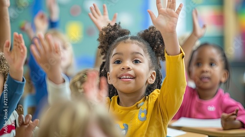 photograph of children 3-4 years old sitting at desks in preschool classroom with hands raised in the air, answering questions  photo
