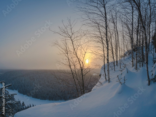 Beautiful sunrise on a frosty morning, a snowy cliff, trees on t