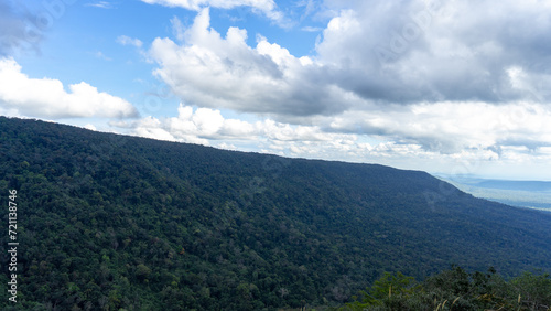 A picture of the view looking down from the top of a mountain. Seeing a fertile green forest below, contrasting with the image of white clouds floating tightly in the sky.