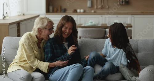 Excited happy grandma, young mother and kid tickling each other, shouting, playing active games on home sofa, having fun together, laughing, enjoying playtime, leisure photo