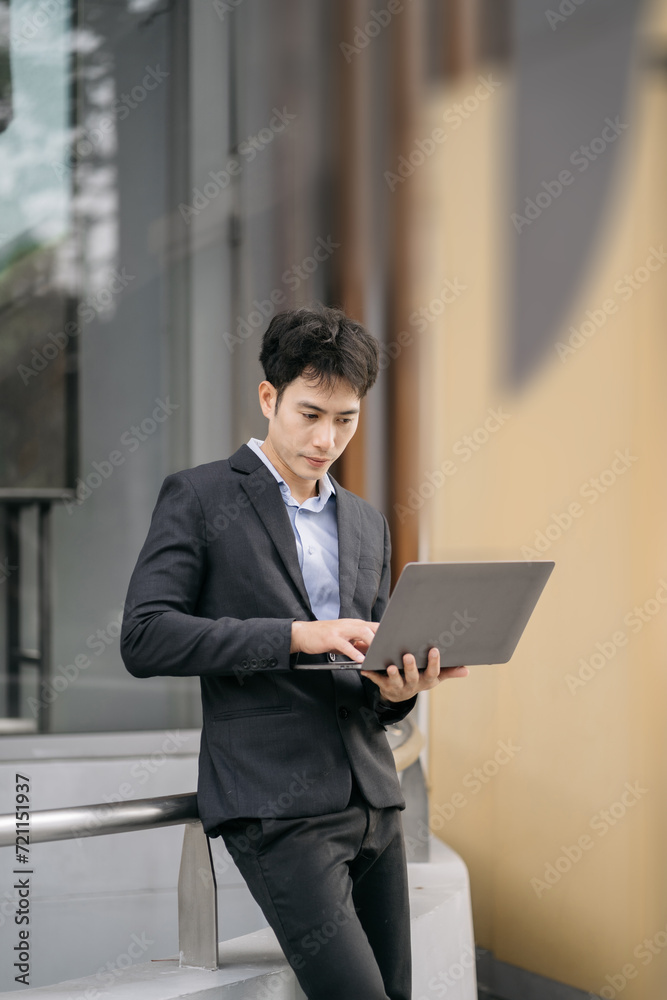 Asian male businessman use smartphone and holding laptop computer, Walk enjoy smiling while doing commuting at business center.