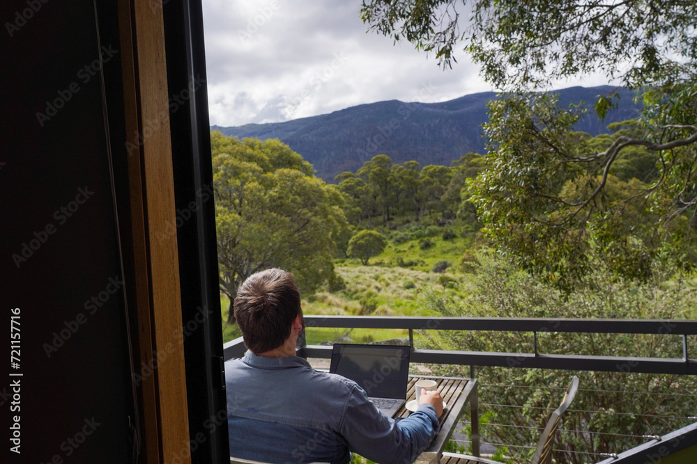 A man working remotely from his balcony looking over bushland and mountains A man working remotely from his balcony looking over bushland and mountains