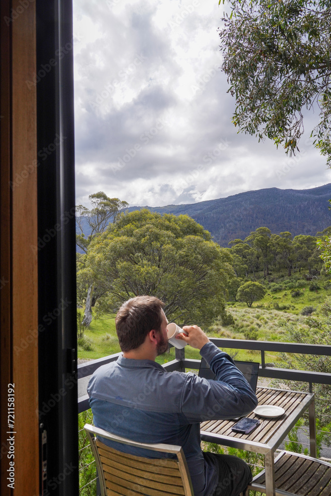 A man working remotely from his balcony looking over bushland and mountains