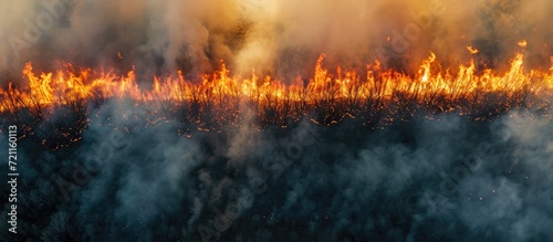 Intense fire and smoke in an open field viewed from above, caused by a tall blaze burning dry grass, creating a natural disaster.
