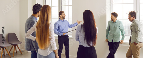 Modern business coach or team manager meeting with a group of diverse people in the office. Male business professional with a clipboard talking to a team of young multiracial people. Banner background photo