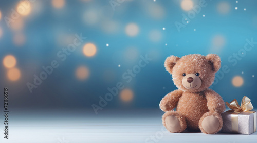 A cute teddy bear sits beside a wrapped gift against a twinkling blue bokeh backdrop.