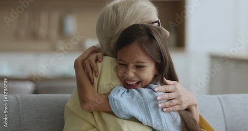 Cheerful grandmother and happy granddaughter girl talking, laughing, hugging with love, tenderness, affection enjoying family close relationship. Joyful kid embracing granny, looking at camera photo