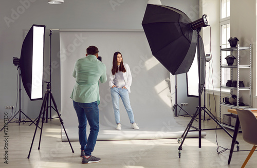 Beautiful model posing for male photographer in studio. Rare view of photographer taking pictures of female model with digital camera in photo studio with professional photographic equipment