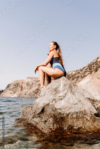 Woman beach vacation photo. A happy tourist in a blue bikini enjoying the scenic view of the sea and volcanic mountains while taking pictures to capture the memories of her travel adventure.