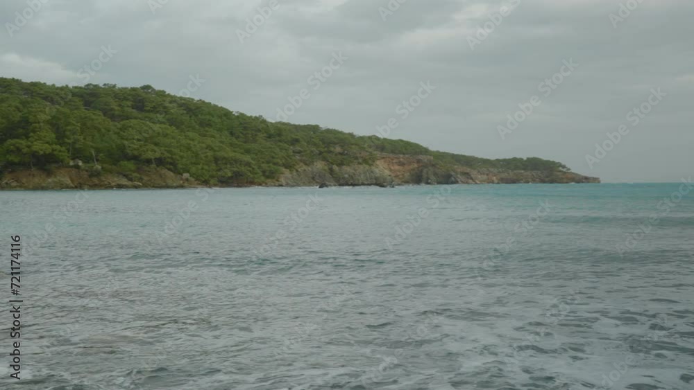 Panorama of a bay with turquoise water, high cliffs, and dense forest on them. Cloudy sky and strong wind. Panorama of a bay with turquoise water, high cliffs, and dense forest on them. Cloudy sky and strong wind.