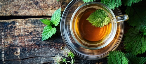 Top view of a cup of herbal tea with fresh stinging nettle leaf on a table.