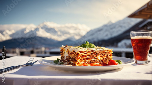 Fototapeta Naklejka Na Ścianę i Meble -  portion of lasagna bolognese with meat sauce in a white plate outdoors in front of a landscape of mountains with snow