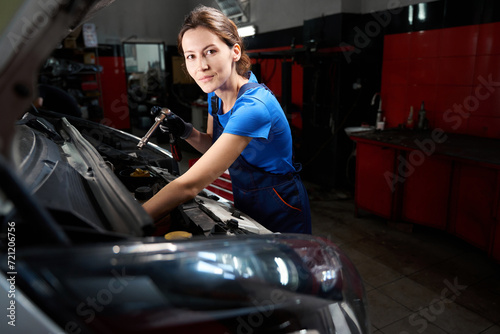 Young woman works under the open hood of a car