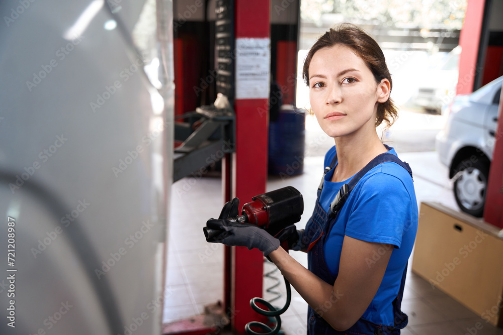 Fototapeta premium Woman auto mechanic works with a car on car lift