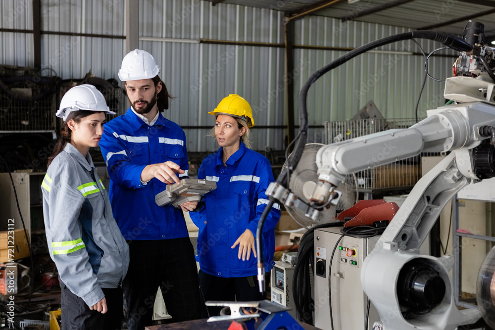 Team engineer using remote robot controller operate standing at automation robot arms machine in factory. technician maintenance robotic workshop. Team engineer using remote robot controller operate standing at automation robot arms machine in factory. technician maintenance robotic workshop.