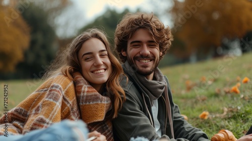 Happy beautiful young couple eating croissant while sitting on the grass on t...