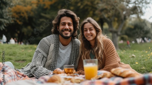 Happy beautiful young couple eating croissant while sitting on the grass on t...