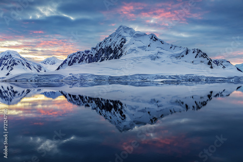 Antartica landscape with sea in the foreground and snow covered mountain in the background with stunning sunset sky all with a amazing reflection in the water