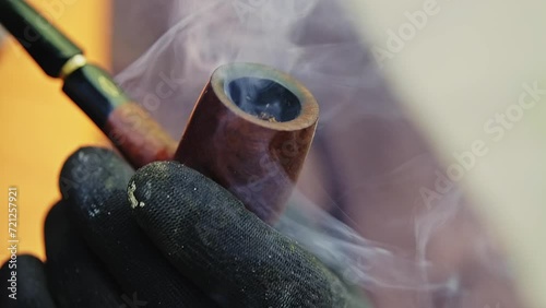 A person wearing black gloves lighting up a wooden pipe .
