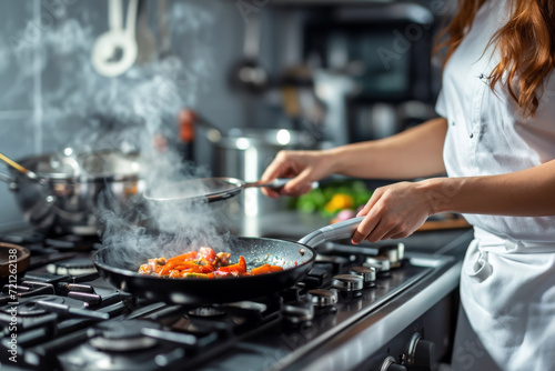 Close up of woman chef with a frying pan cooking on a modern kitchen stove. Working concept of cooking and food.