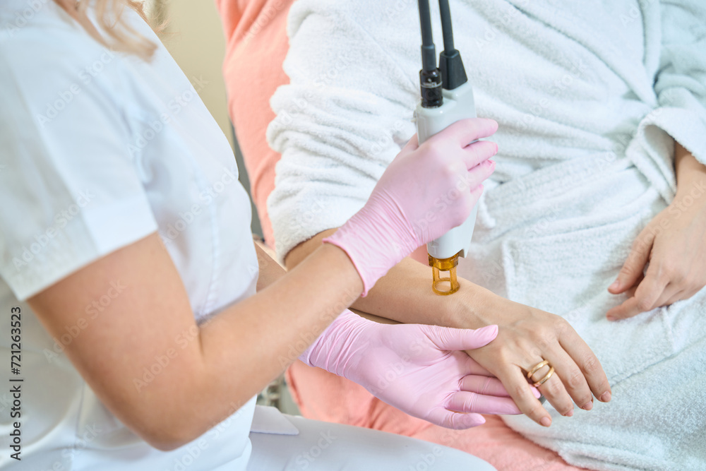 Partial image of female cosmetologist doing laser epilation of woman hand