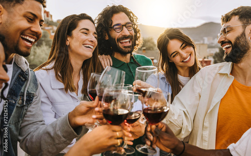Happy friends toasting red wine glasses outside - Group of young people having bbq dinner party in backyard house - Winery and bbq dining concept with guys and girls cheering alcohol together photo