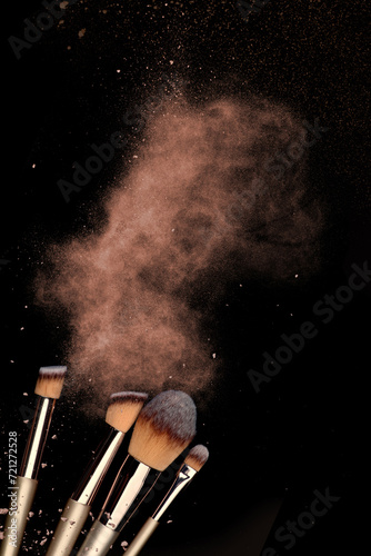 Explosion of shimmer, bronzer, highlighter powder dust, eye shadow, blush brushes on black background. Pigments for make-up. Abstract background for cosmetic makeup concept