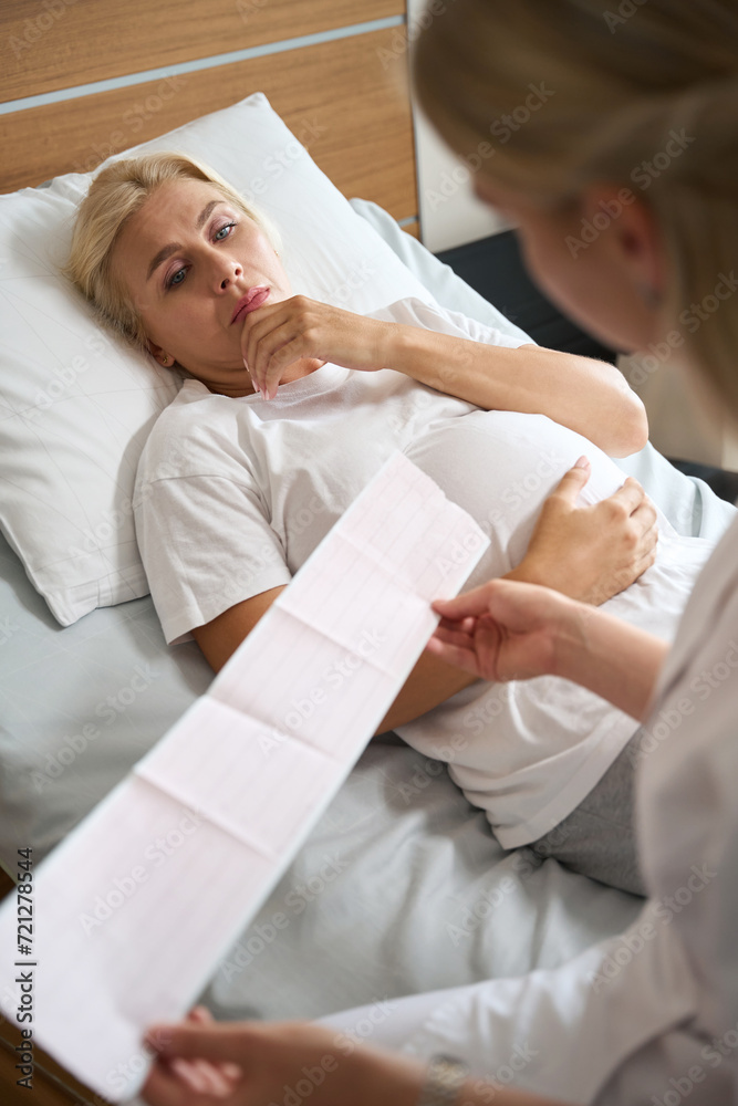 Pregnant woman looking at her electrocardiogram in hands of female nurse Pregnant woman looking at her electrocardiogram in hands of female nurse