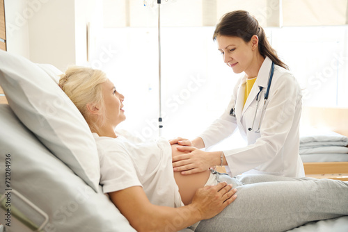 Focused female nurse checking pregnant belly of european woman